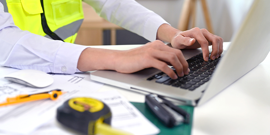 Cropped view foreman engineer or architecture's hand working on a laptop with tools and machine on the table in the office, for engineering, architect, business, safety and technology concept.